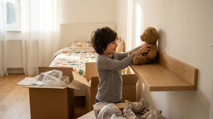 A young child placing favourite toys onto a shelf in their freshly set-up bedroom after moving into a new home