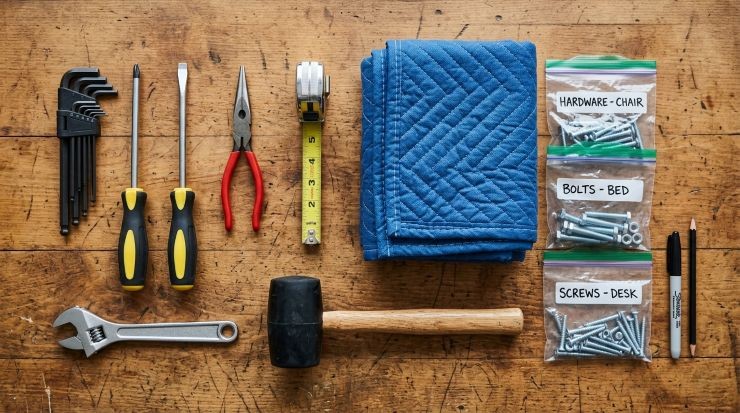 Set of essential tools for furniture disassembly including screwdrivers, Allen keys, wrench, hammer, and measuring tape neatly arranged on a wooden surface