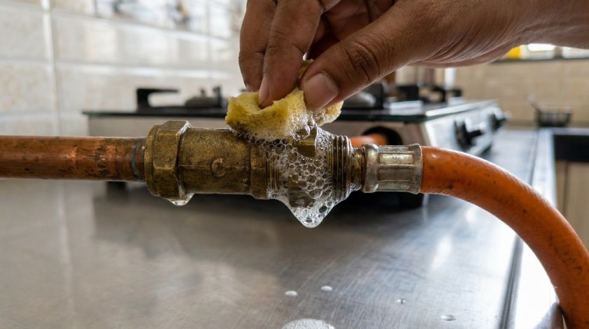 Soapy water applied to kitchen gas pipe joint showing bubbles that signal an active leak