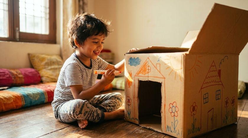 Child drawing on a large cardboard box turned into a playhouse