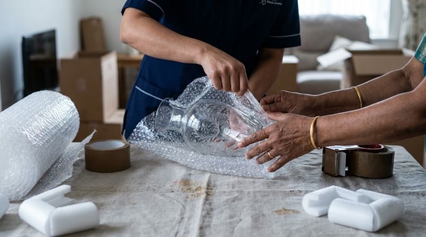 Professional movers carefully wrapping fragile glassware and antiques in bubble wrap before loading them onto the truck