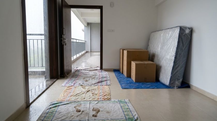 Old towels and sheets laid across the floor inside the doorway of a new flat with cartons staged beside the entrance
