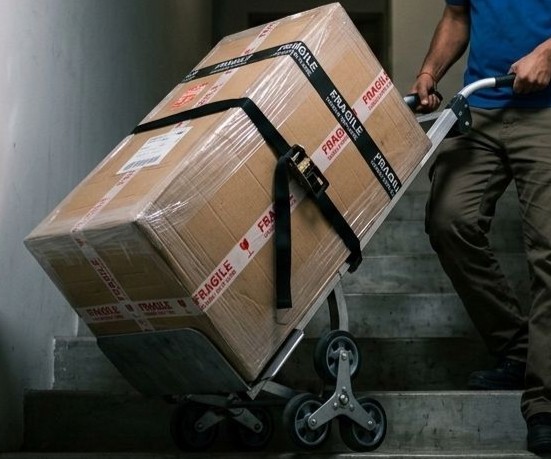 A stair climbing dolly with a tri-star wheel mechanism carrying a heavy item down a narrow apartment staircase